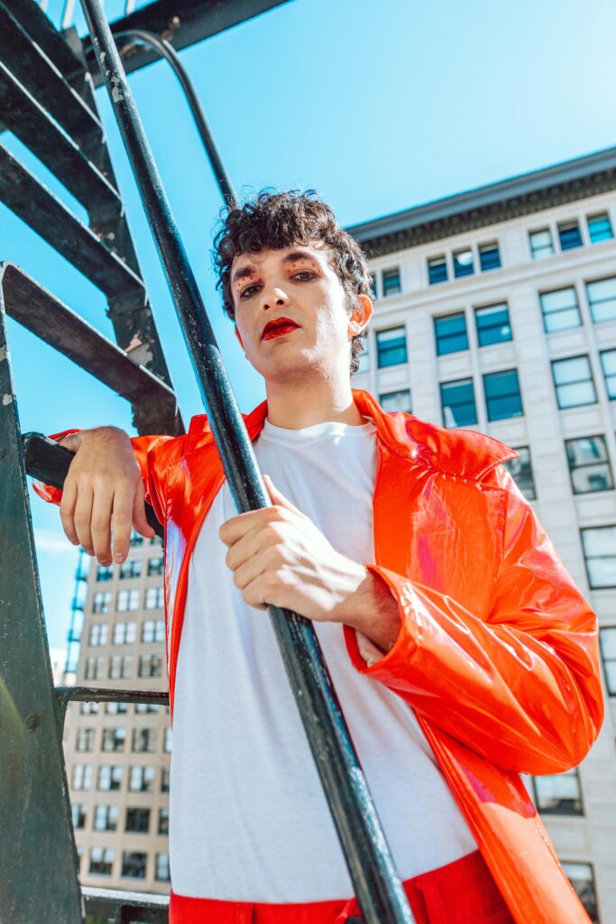 Stylish person in a vibrant red jacket posing outdoors against an urban backdrop.