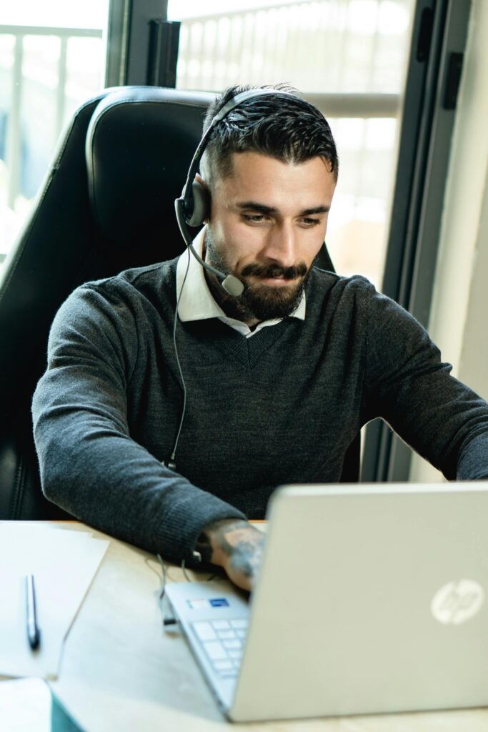 Business professional with a beard using a laptop and headset at work.